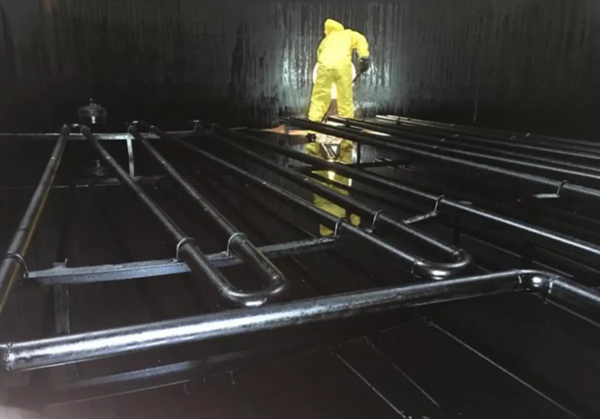 Técnico com EPI na limpeza interna de um tanque com serpentinas de aquecimento